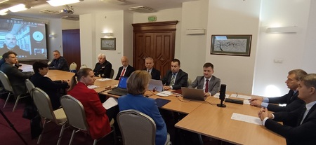  Drugie posiedzenie Rady Metrologii II kadencji w Kielcach.  uczestnicy siedzą przy stole w sali konferencyjnej słuchając wystąpienia prelegenta.