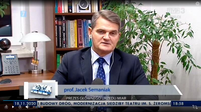 Klatka materiału telewizyjnego: przy biurku siedzi rozmówca - prezes GUM profesor Jacek Semaniak. Przed sobą ma mikrofon. Jest ubrany w garnitur i krawat, ma słuchawki w uszach. Poniżej podpis oraz pasek z wiadomościami.