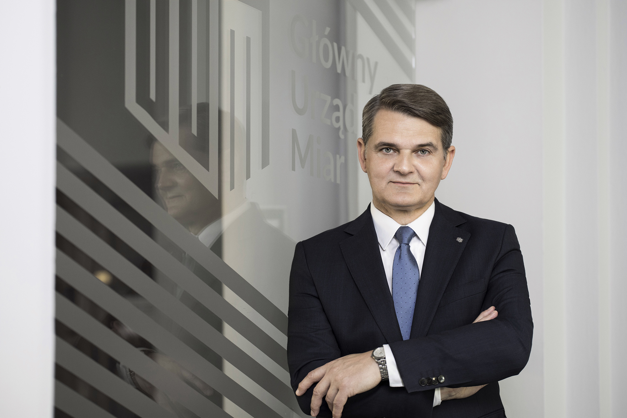 Prezes Głównego Urzędu Miar - prof. Jacek Semaniak. Na zdjęciu widoczna sylwetka mężczyzny w wieku średnim, w czarnym garniturze, białej koszuli i w niebieskim krawacie.